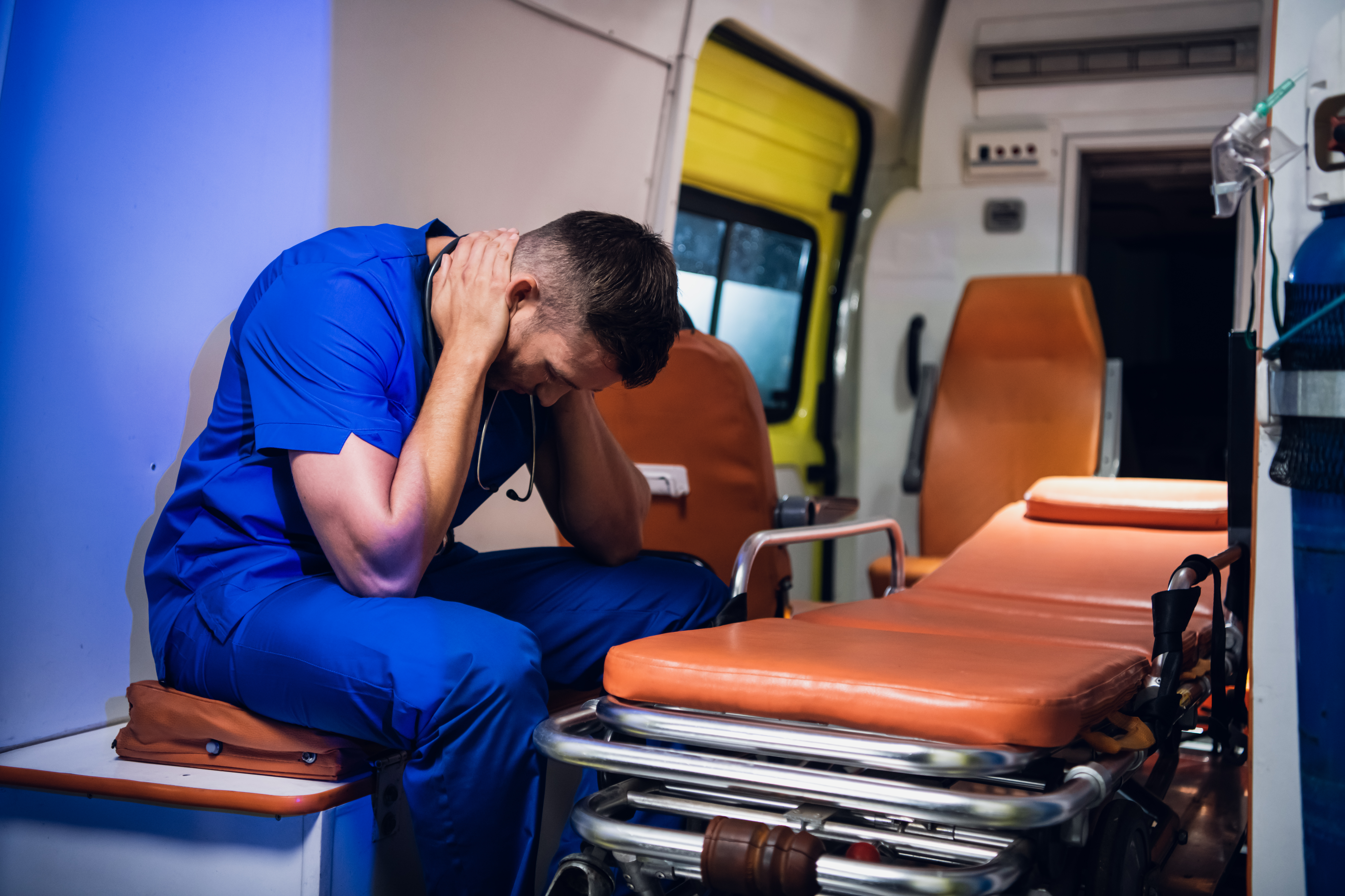 An exhausted paramedic having a little break by sitting in an ambulance with his hands around his neck | Source: Shutterstock