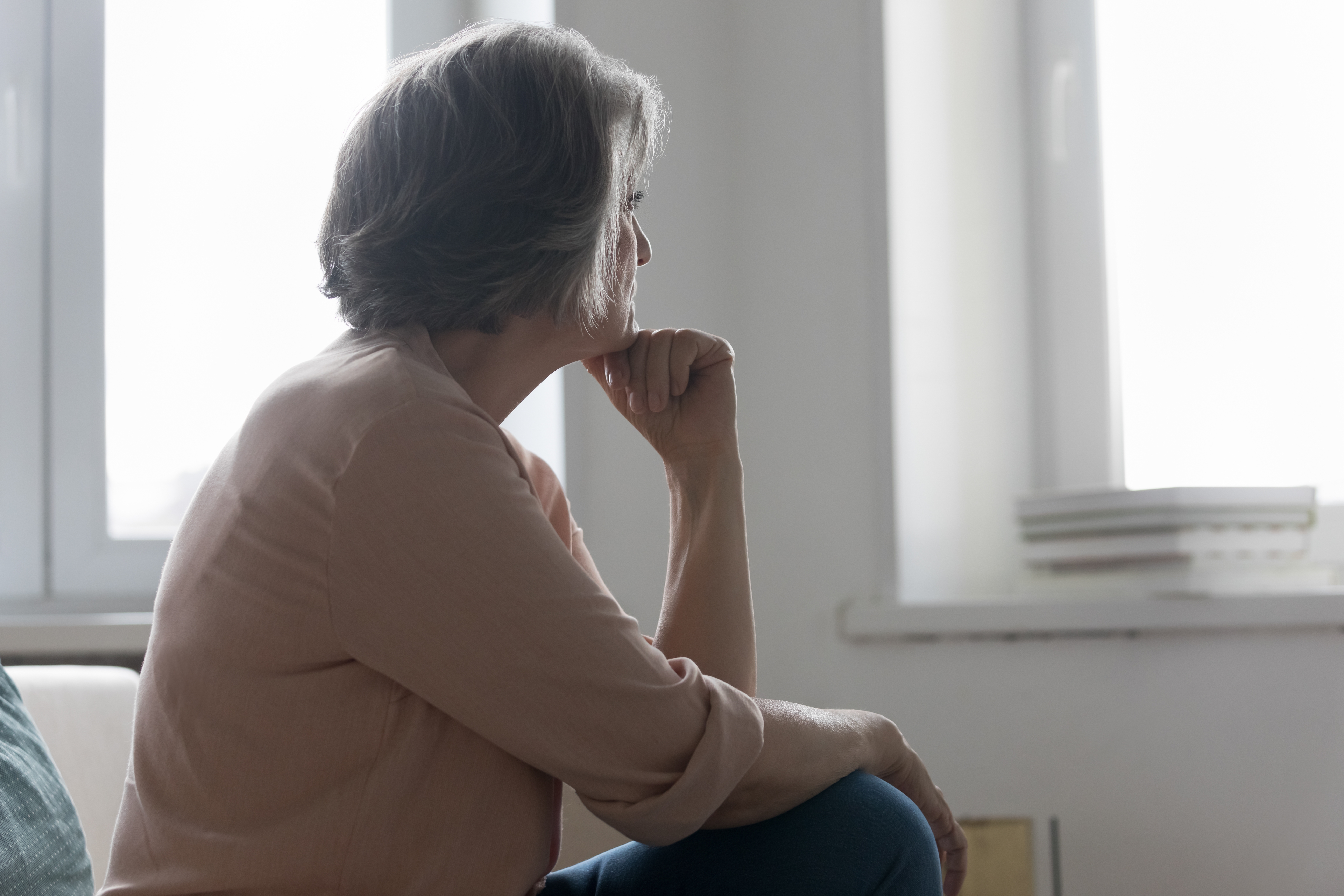An older woman sitting on a bed and looking outside thoughtfully | Source: Shutterstock