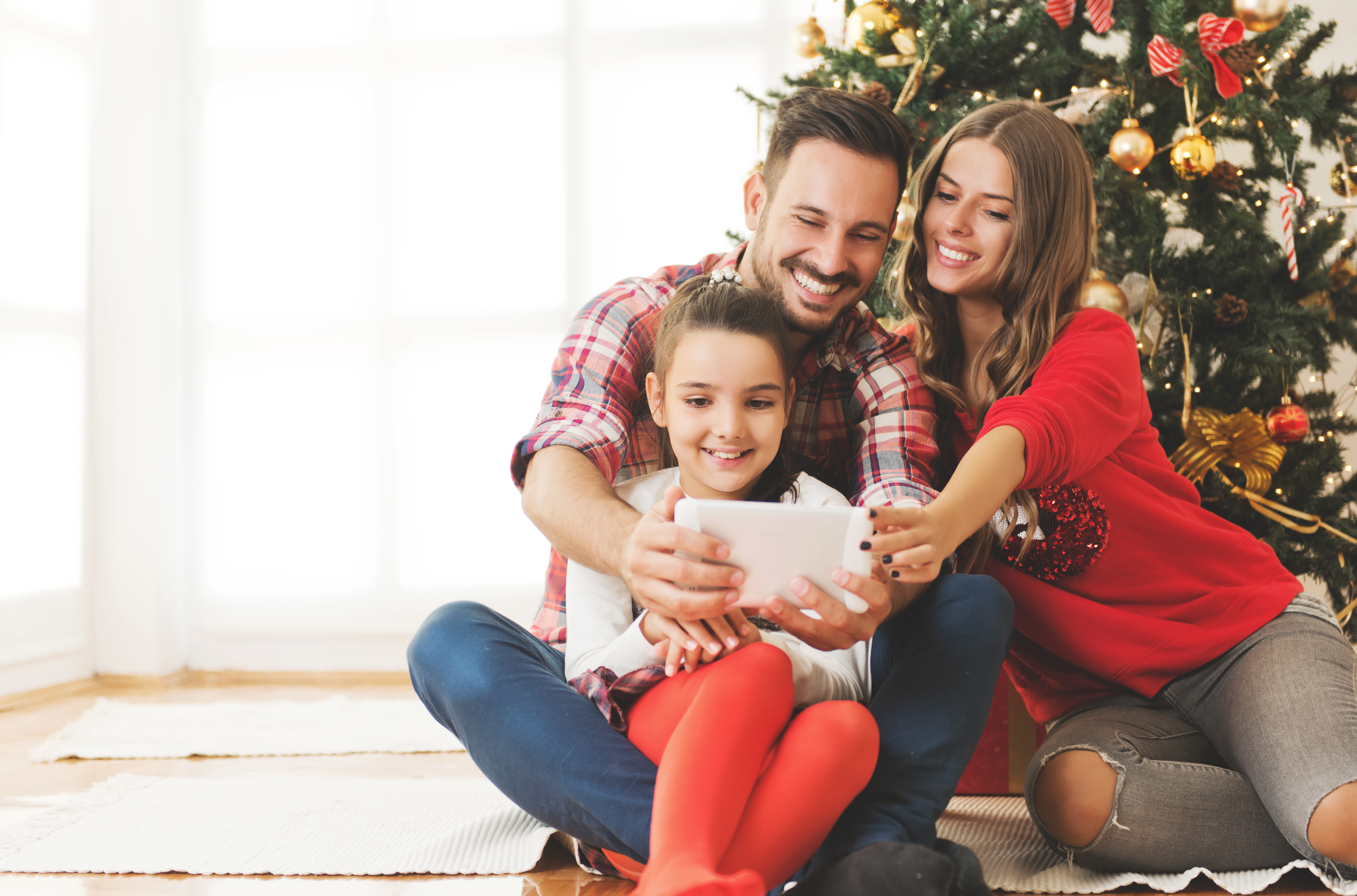 A little girl playing with an iPad with her father and mother with a Christmas tree in the background | Source: Shutterstock