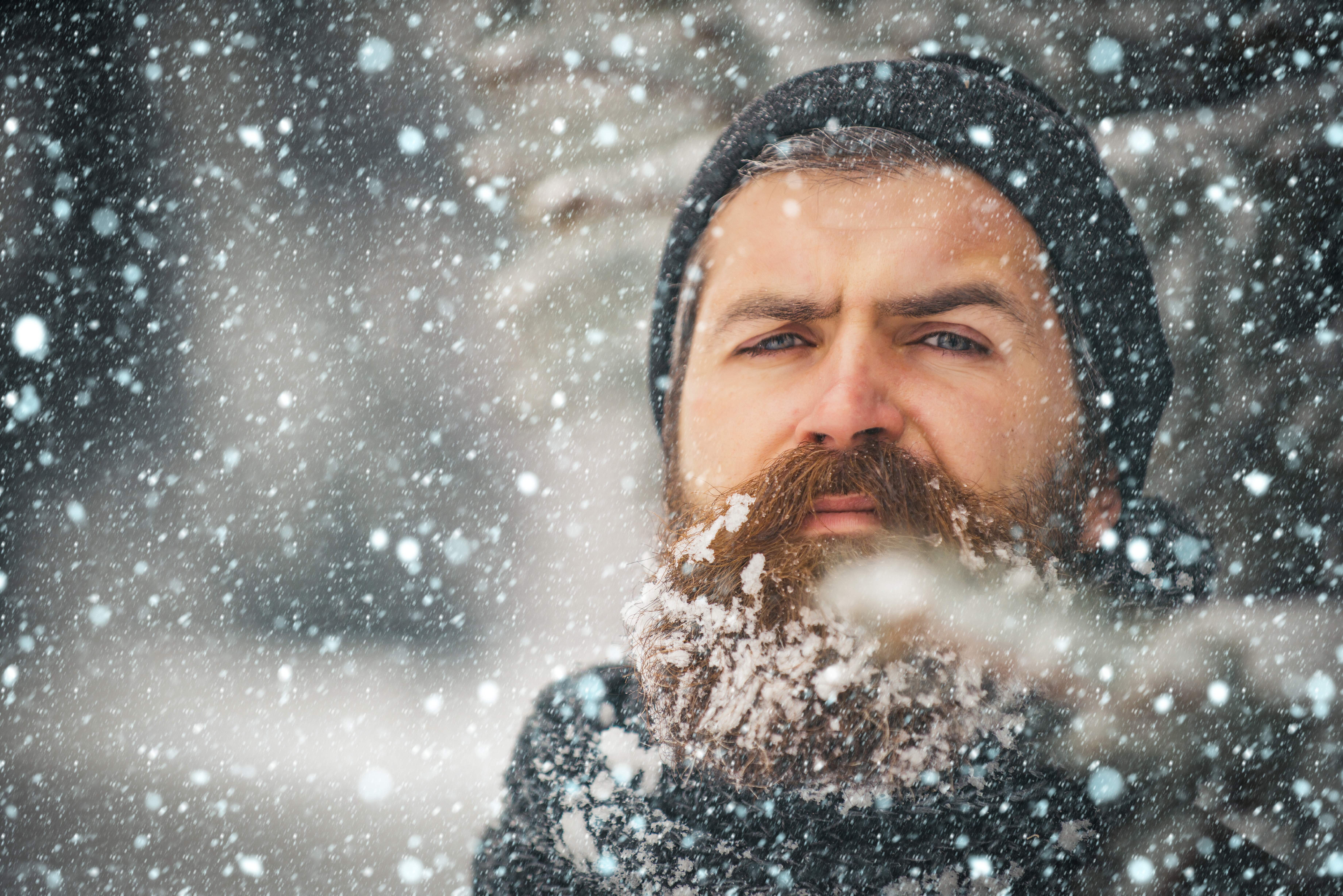 A man with a beard and hat, standing outside as snow falls | Source: Shutterstock
