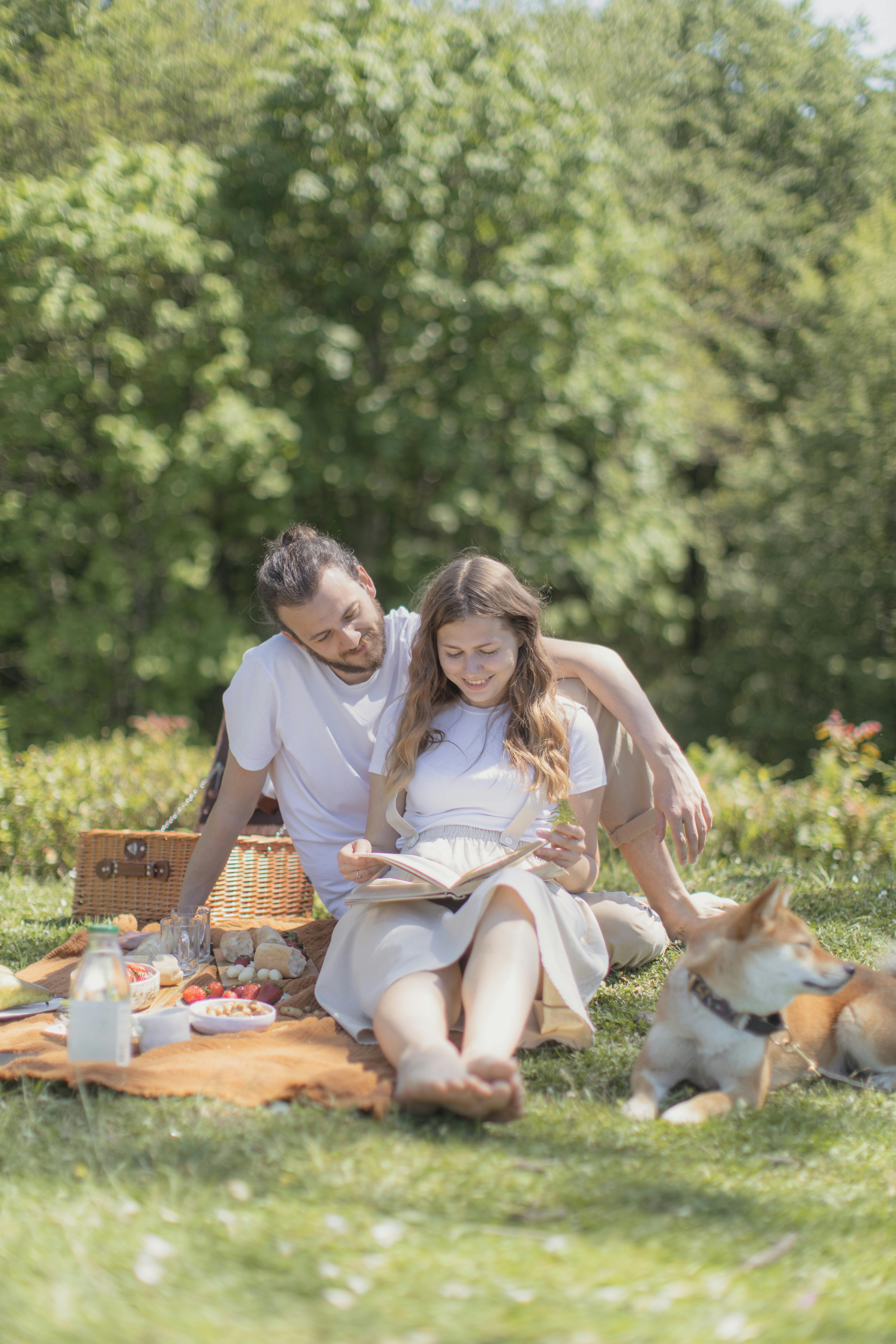 Couple sitting on a picnic mat with a dog | Source: Pexels